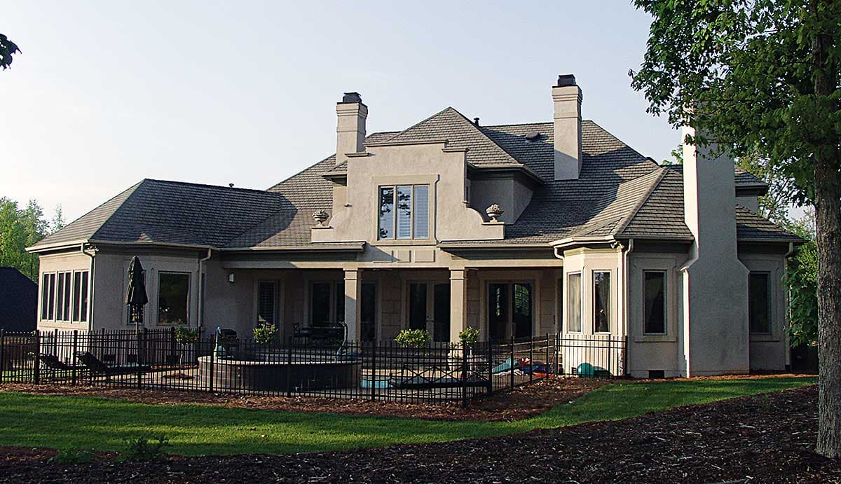 House plan exterior: Two-story stucco home with multiple gables, dual chimneys, and a covered rear porch.