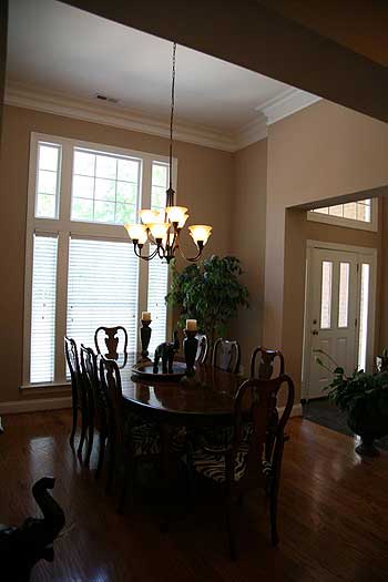 Dining room with large multi-pane windows, chandelier, oval table, and double doors leading to entryway.