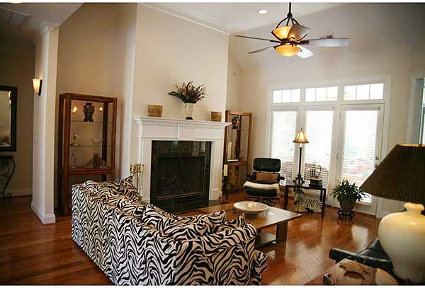 Living room with fireplace, vaulted ceiling, ceiling fan, large windows, and wood floors.