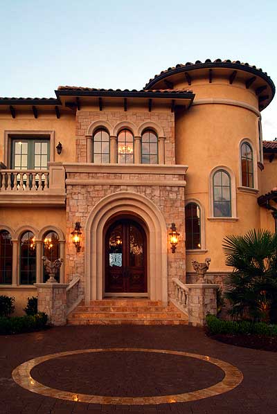 Mediterranean style house plan exterior with arched entryway, stone accents, turret, and balcony.