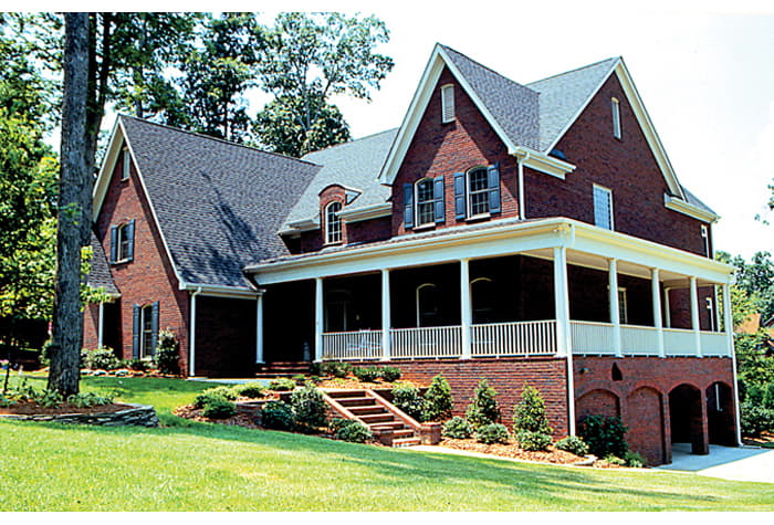 House plan exterior: two-story brick home with wraparound porch, multiple gables, dormer windows, and arched garage openings.
