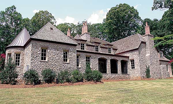 House plan exterior with stone walls, conical turret roof, gables, dormers, and arched covered entryway.