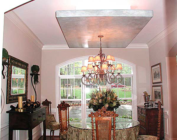 Dining room with arched window, ornate chandelier, glass-top table, and decorative buffet.