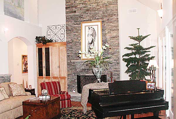 Living room interior with stacked stone fireplace, grand piano, armoire, and seating.