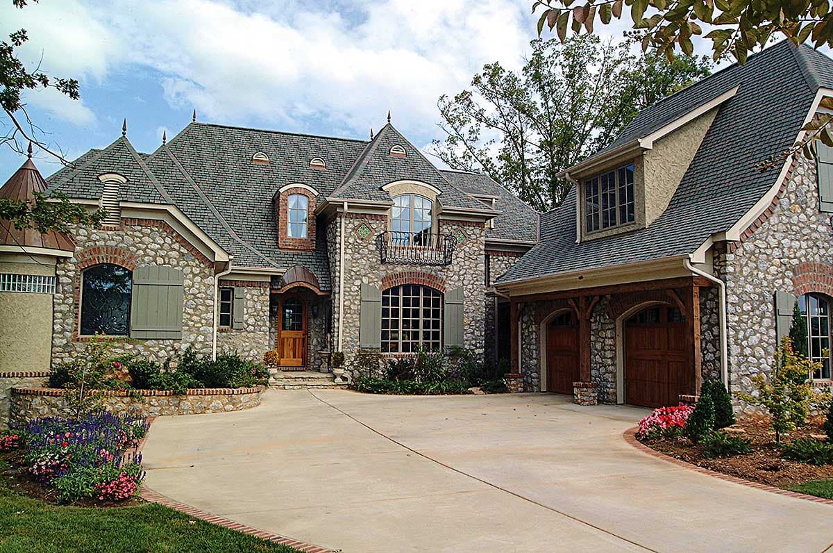 House plan exterior: French Country style, stone and stucco facade, multi-level roof with dormers, arched entry, and attached three-car garage.
