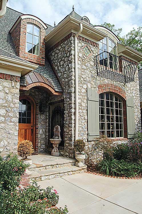 House plan exterior with stone facade, arched entryway with copper roof, dormer window, and balcony.