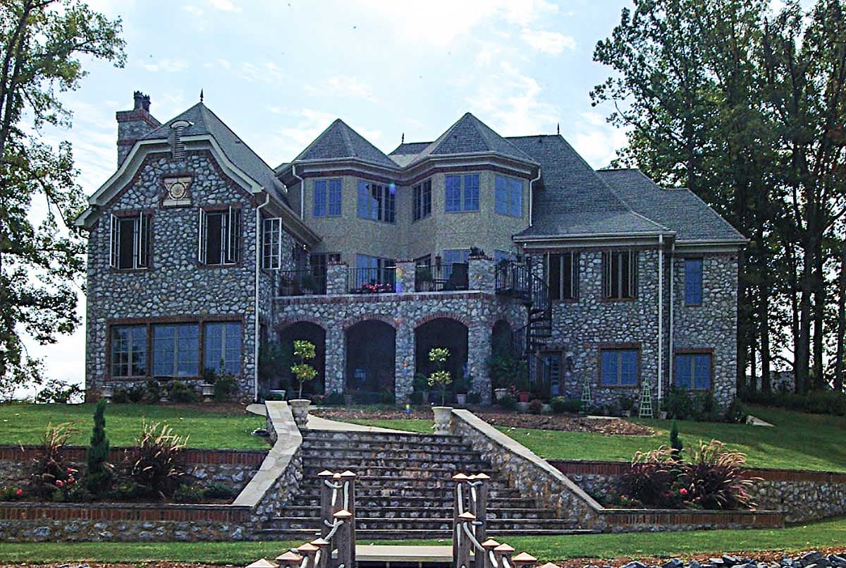 House plan exterior: multi-story stone residence with arched loggia, multiple gables, dormers, and spiral staircase.