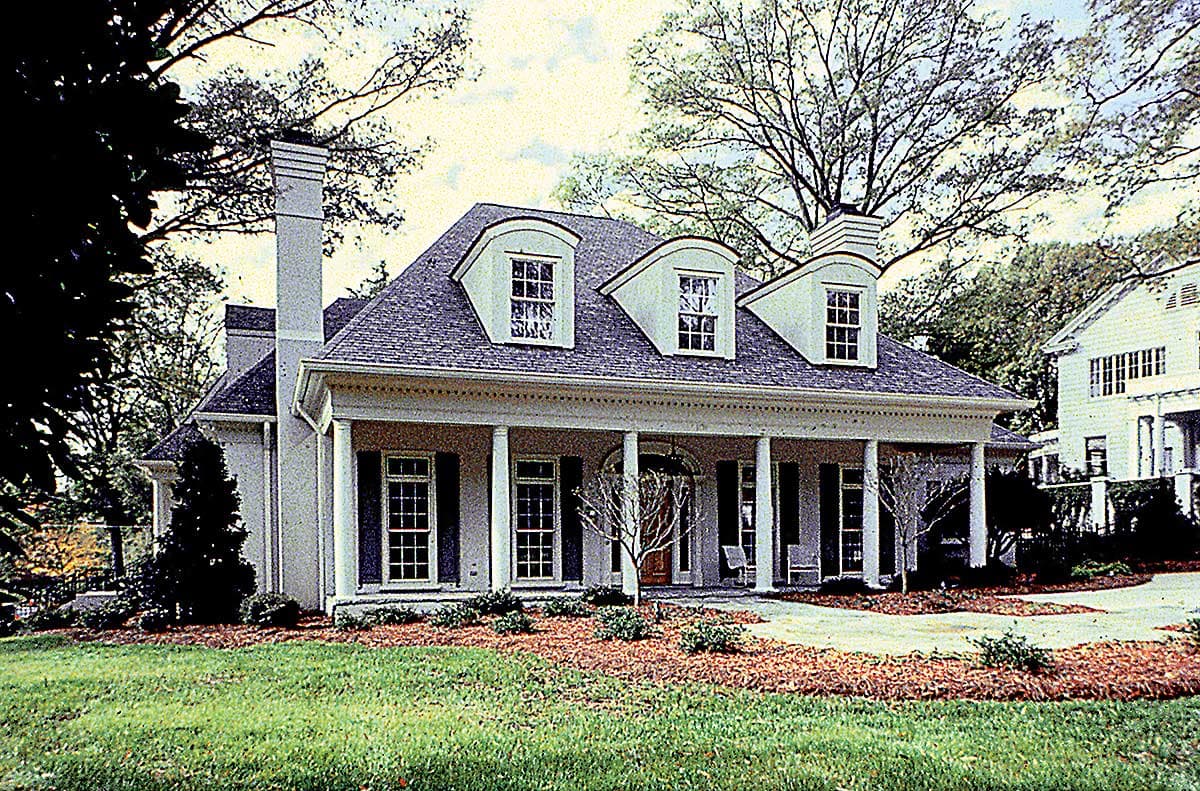House plan exterior with a broad covered porch supported by columns, dormer windows, and a prominent chimney.