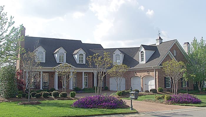 Two-story brick house plan with front porch, multiple dormers, arched garage bays, and a cupola.