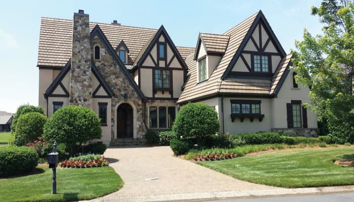 Tudor-style house plan exterior with stone chimney, multiple gables, dark trim, and wood shingle roof.
