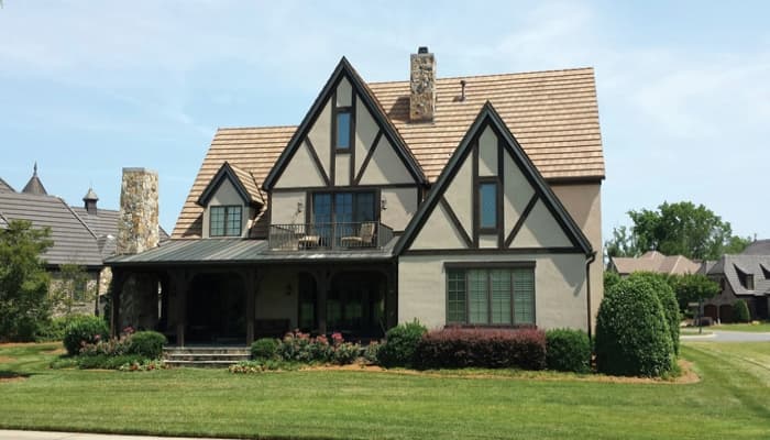 Tudor style house plan exterior with steeply pitched gables, stone chimney, covered porch, and second-story balcony.