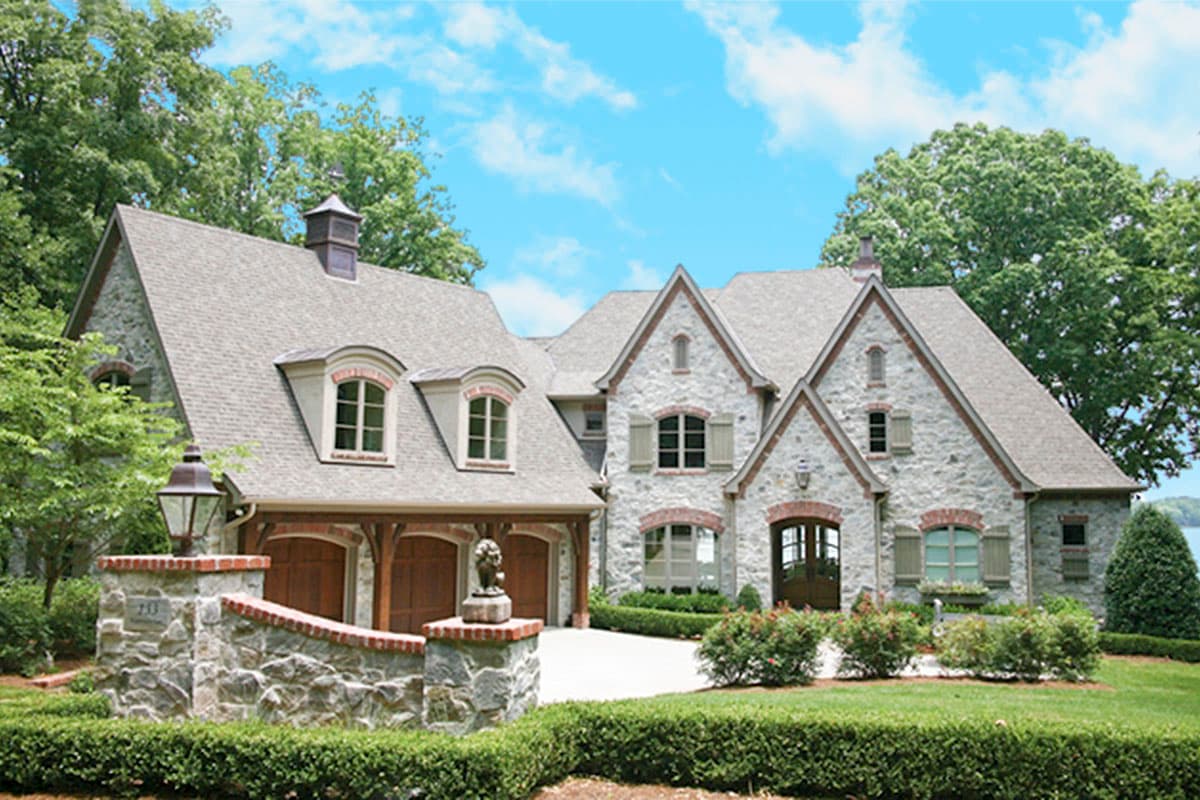 House plan exterior with stone facade, multiple gables, dormer windows, and a three-car garage with wooden doors.