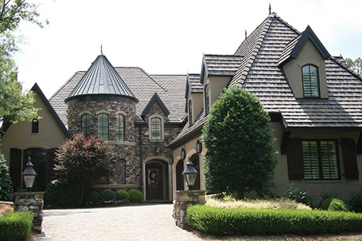 House plan exterior featuring stone facade, conical turret roof, multiple gables, and arched windows.