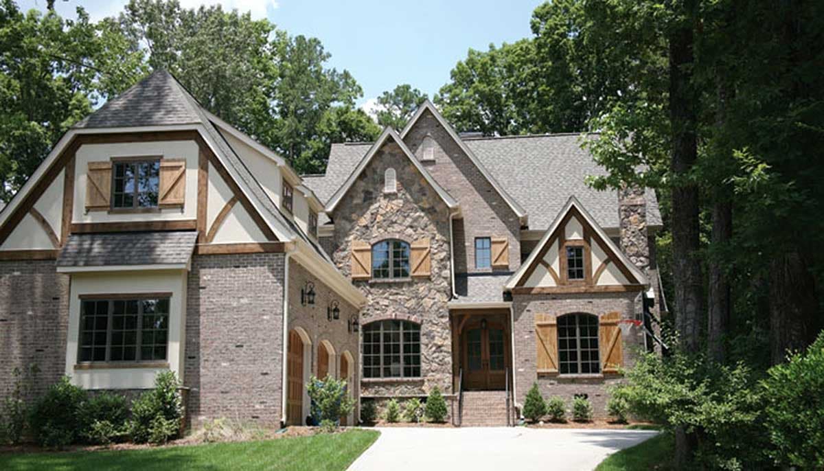 House plan exterior features stone accents, multiple gables with timber framing, and a side-entry garage. Two stories with a steep roofline.