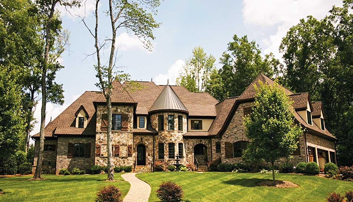 House plan exterior with stone facade, turret, multiple gables, and dormers. Features a stone walkway and manicured lawn.