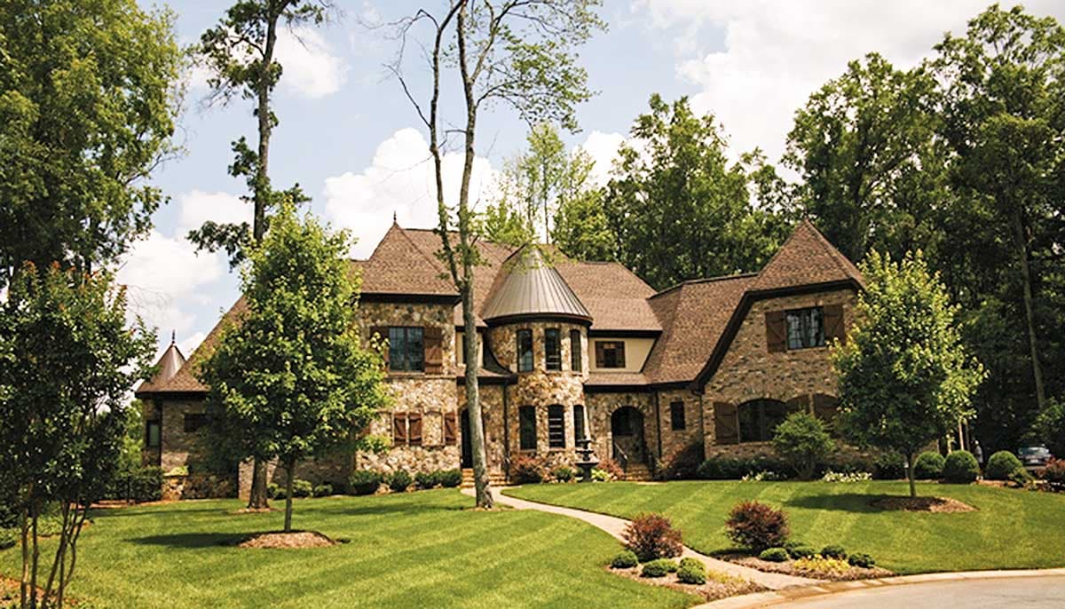 Stone Tudor-style house plan exterior with multi-level gables, a conical tower, and stone facade.