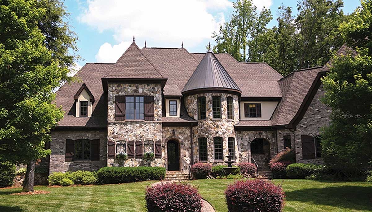 House plan exterior: stone and brick facade, multiple gables, dormers, and a conical turret roof.