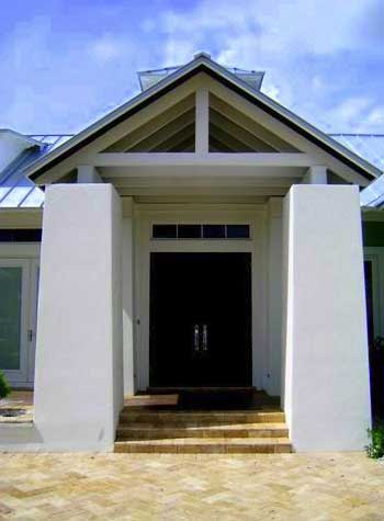 House plan exterior with a modern tropical style, featuring a covered entry with exposed rafters, white stucco pillars, and a metal roof.
