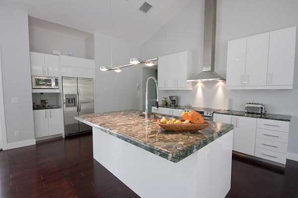 Modern kitchen with a large island, stainless steel appliances, and white cabinetry. Vaulted ceiling with pendant lighting.