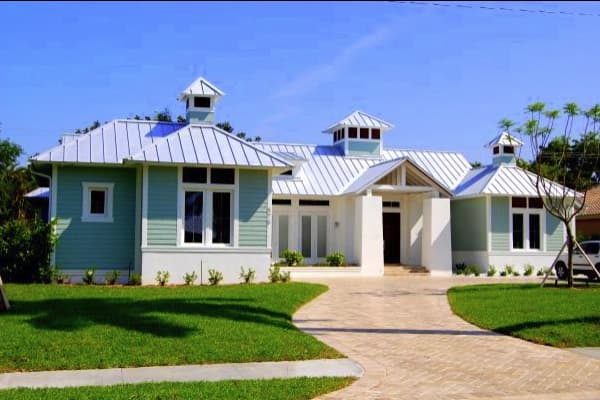 House plan exterior of a single-story home with a metal roof, multiple gables, and cupolas. Features horizontal siding and a covered entry.