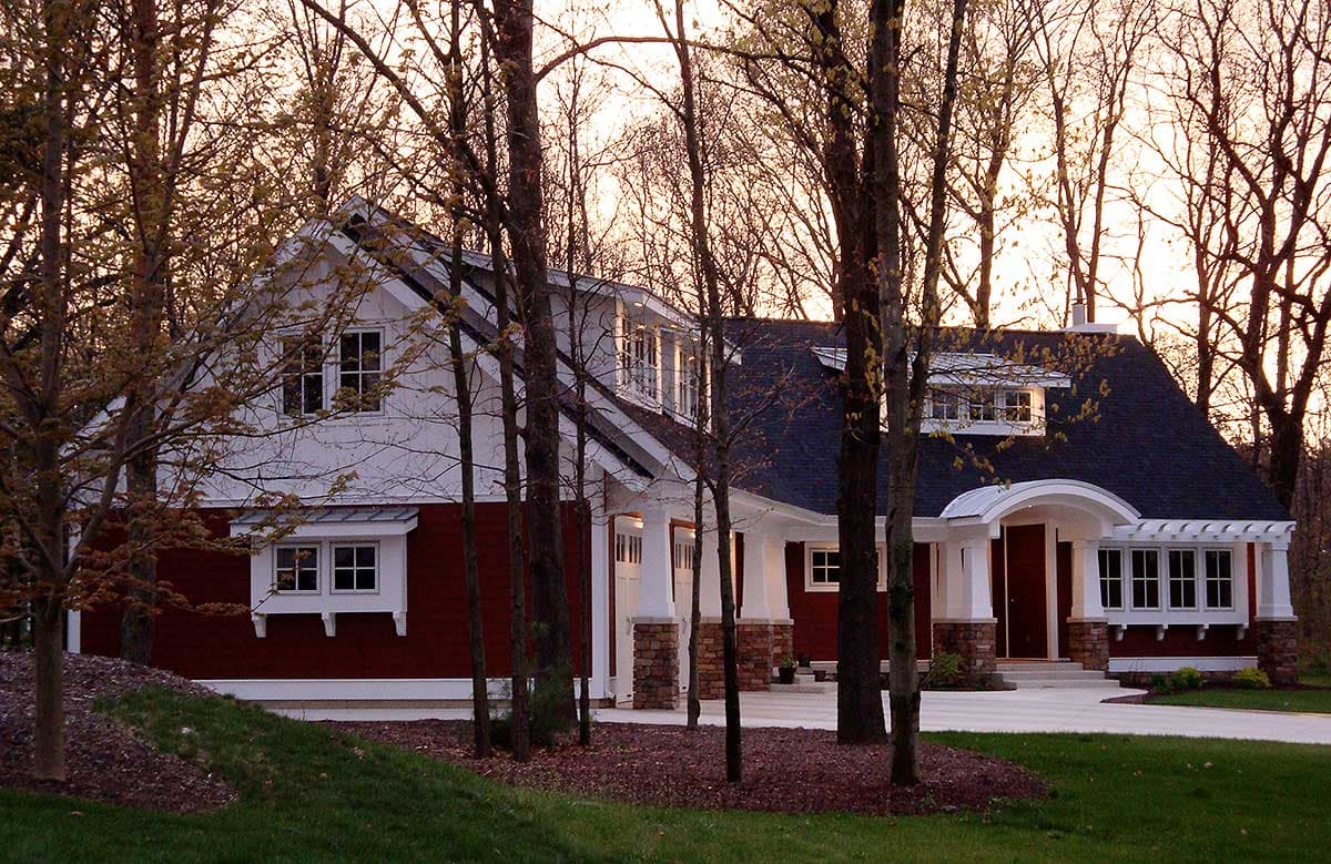 House plan exterior: Two-story, red siding, white trim, prominent gables, dormer windows, and a covered entry with arched pergola.