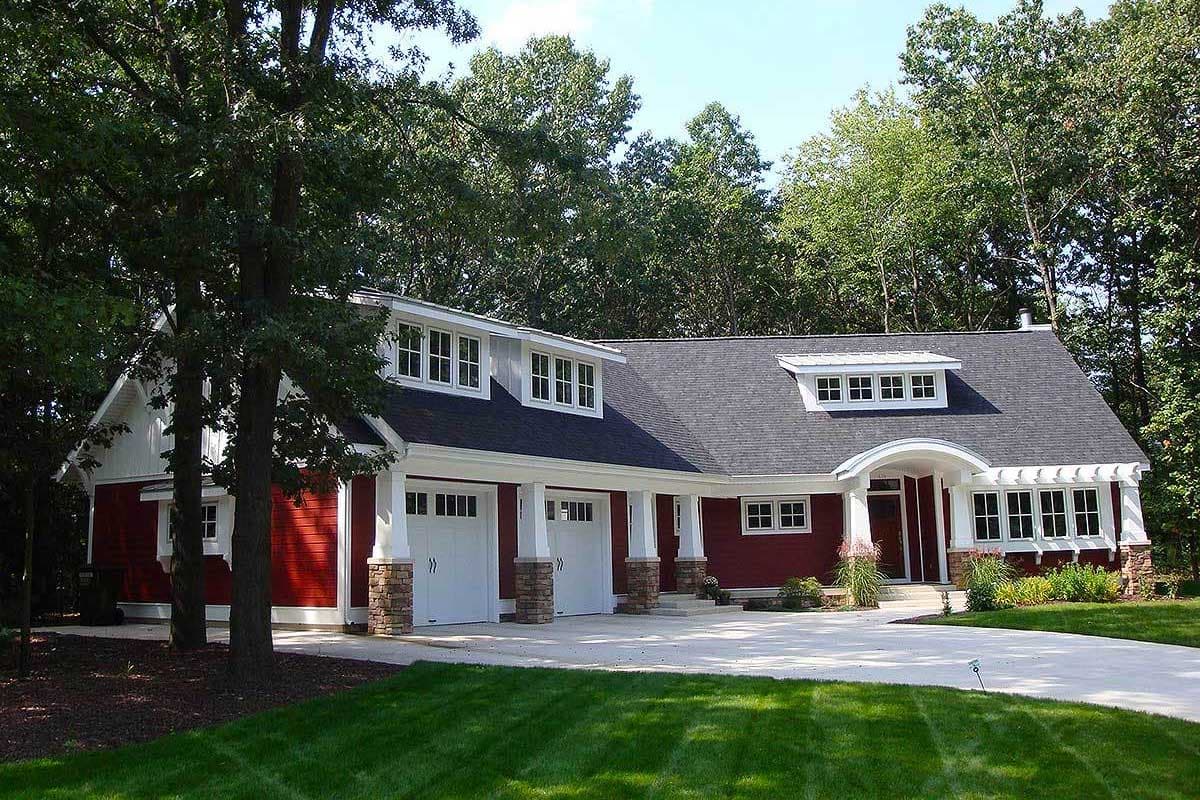 House plan exterior: Red, 1.5-story home with three-car garage, dormers, and arched entry porch.