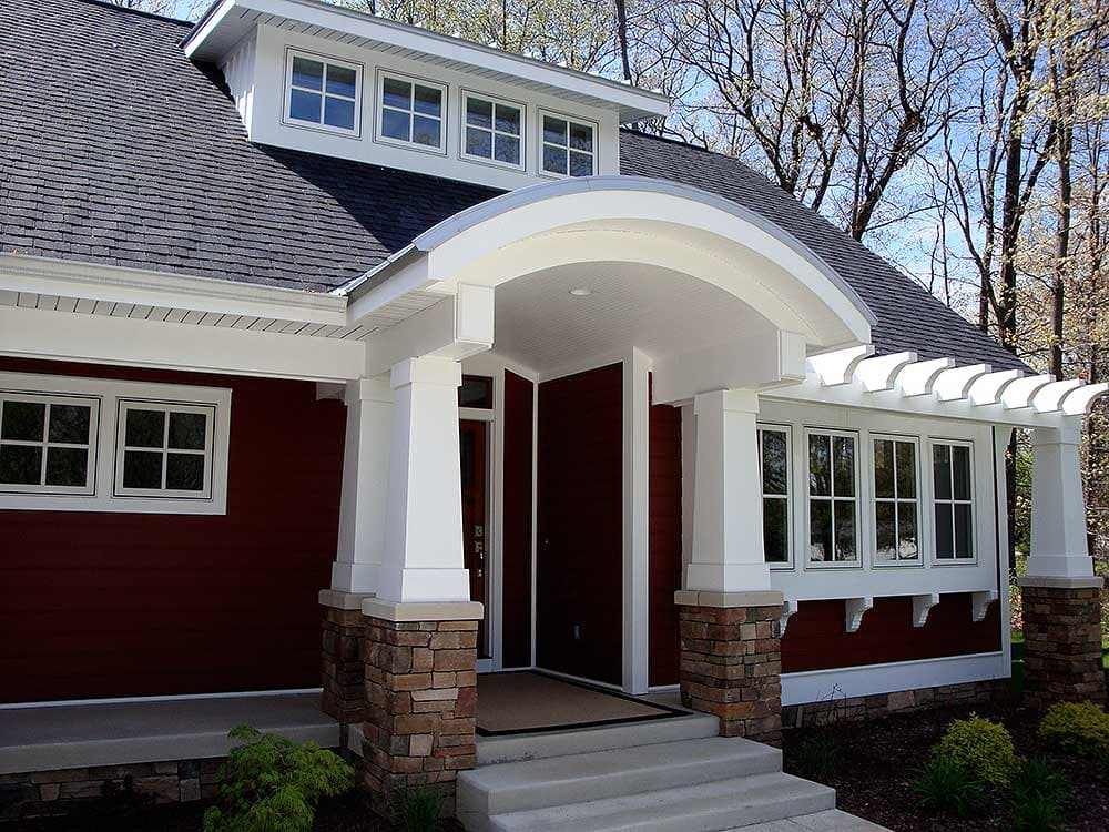 House plan exterior with a covered arched entry, stone-clad columns, and multiple dormer windows.