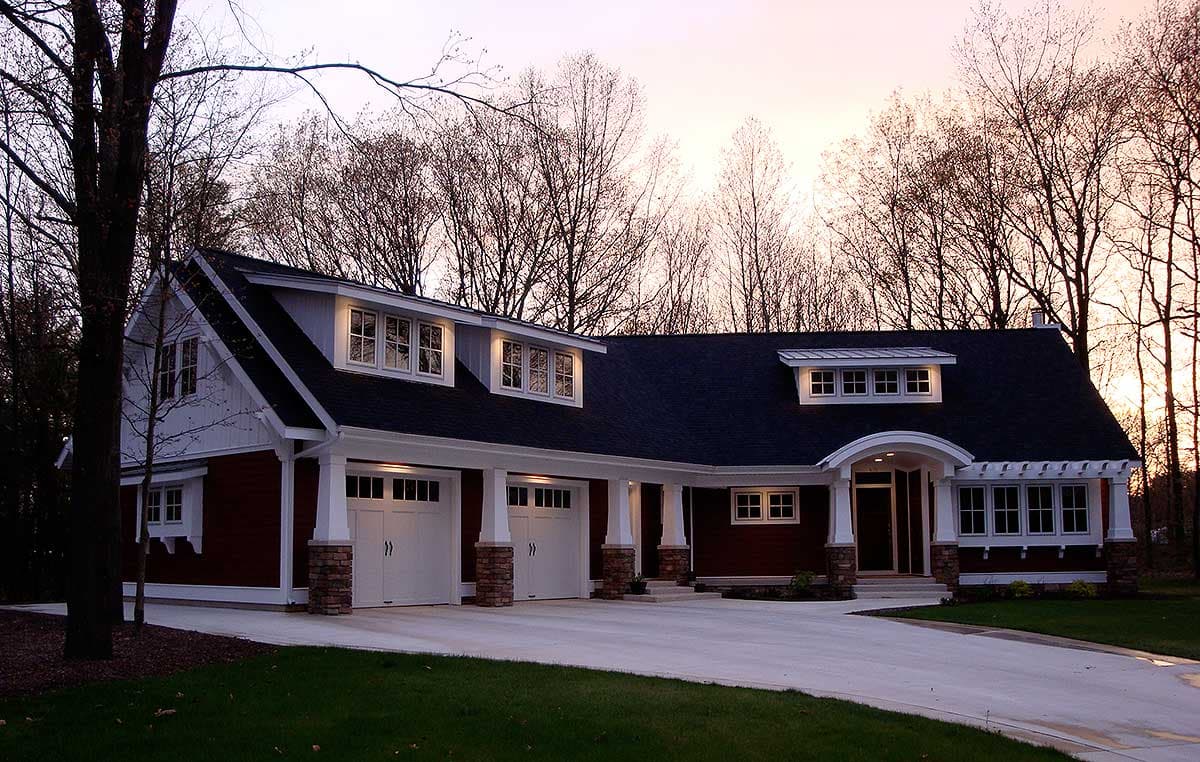 House plan exterior of a two-story home with a dark roof, white trim, three-car garage, and arched entry with dormer windows.