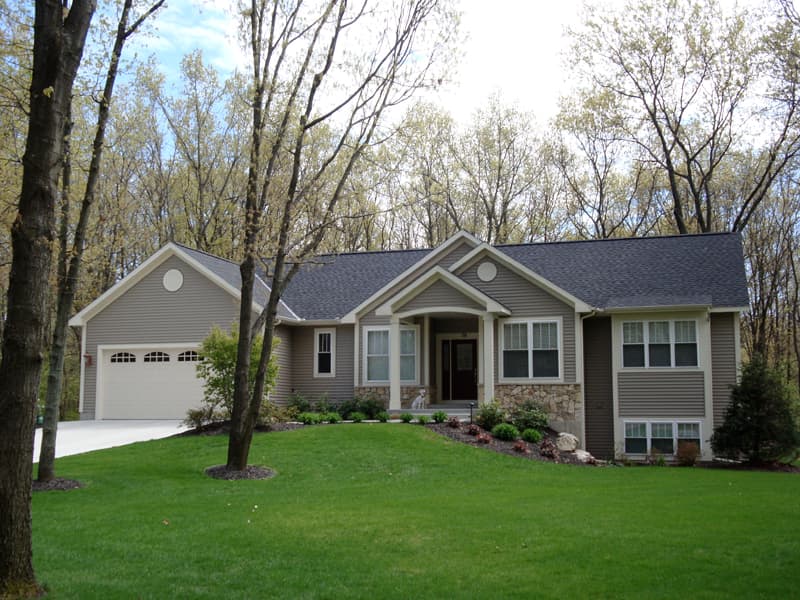House plan exterior featuring a one-story home with attached garage, covered entry porch, gabled dormer, and stone accents.
