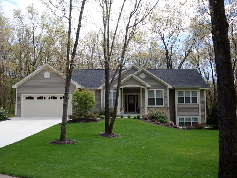 House plan exterior: Ranch style, neutral siding, stone accents, covered entryway, and attached garage with arched windows.