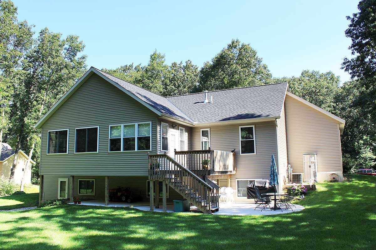 House plan exterior: two-story home with gabled roof, vinyl siding, large deck, and exposed lower level.