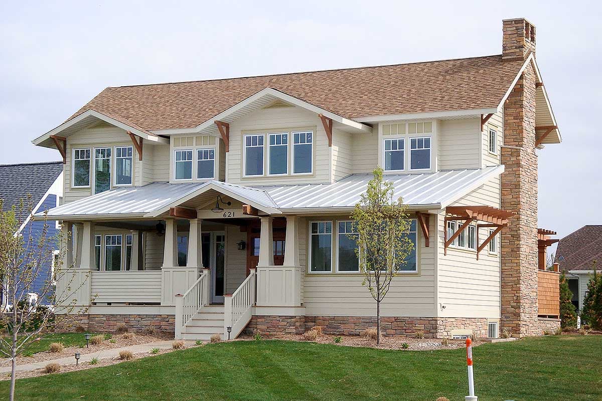 House plan exterior. Two-story Craftsman home with a metal roof, front porch, and exposed rafter tails. Features a stone chimney and shake siding.