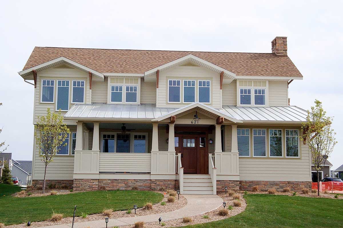 House plan exterior: two-story home with gabled dormers, metal roof accents, stone base, and a covered front porch with square columns.