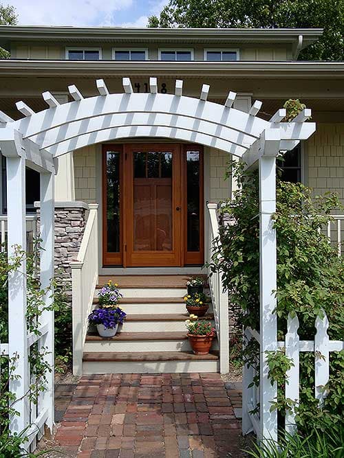 Craftsman style house exterior with white pergola over front door, stone accents, and multipane windows.