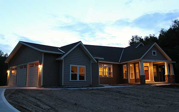 House plan exterior: single-story, modern farmhouse style with a three-car garage, covered front porch with stone-clad columns, and multiple gables.