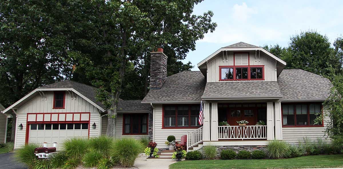 Craftsman style house plan exterior with a porch, stone chimney, and attached garage. Features wide eaves and red trim.