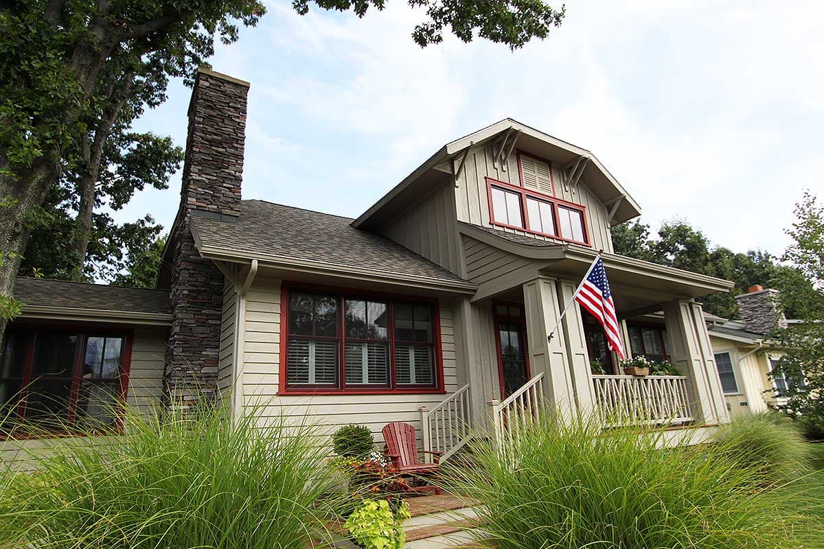 Craftsman style house plan exterior with stone chimney, gables, dormers, and covered porch with railing.