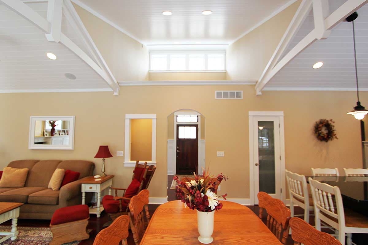 Interior view with vaulted ceiling, exposed beams, and open layout. Dining table, living area, and doorway visible.