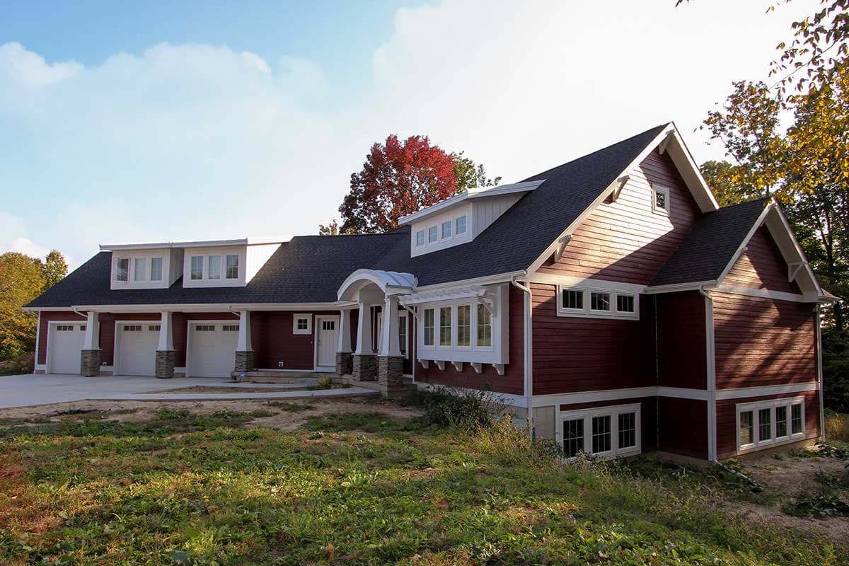 House plan exterior of a multi-story home with a four-car garage, covered entryway with stone pillars, and multiple dormers.