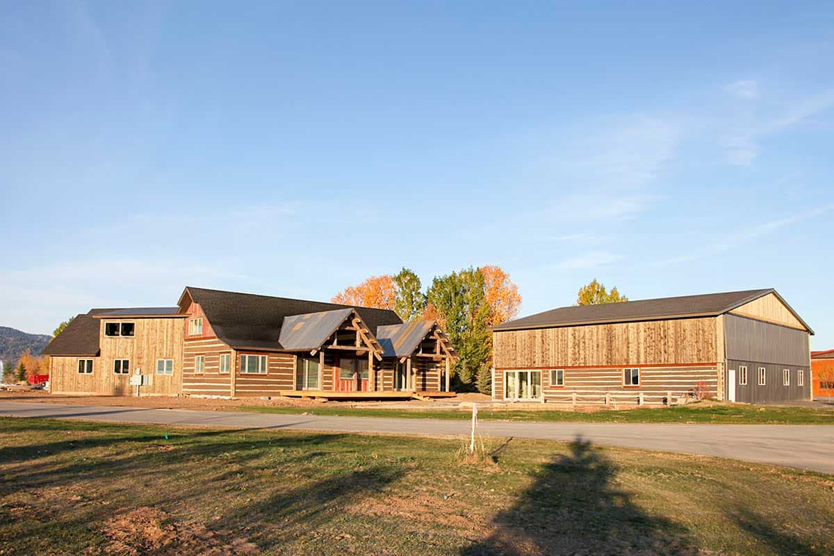 Log cabin house plan exterior with two stories, a large porch, and a separate barn structure.