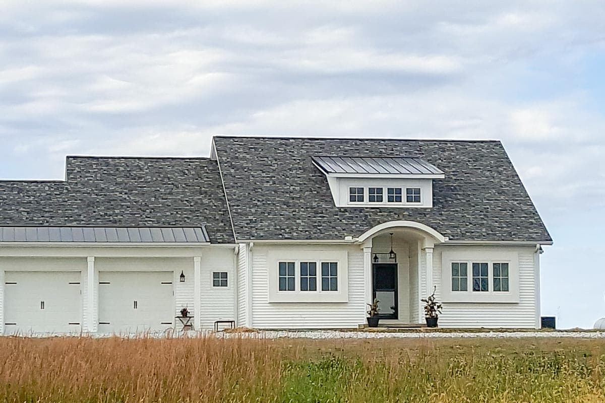 House plan exterior: White siding, gabled roof with metal dormer, arched entryway, and three-car garage.