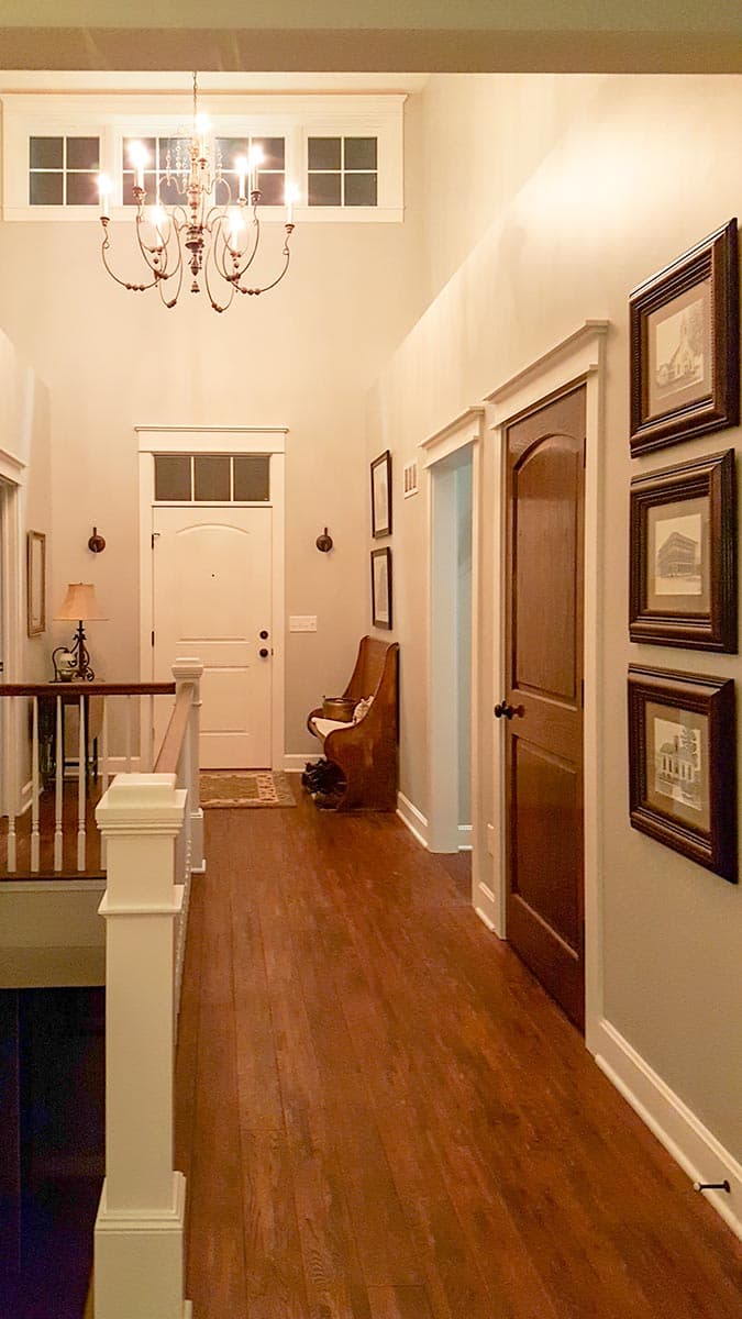 Interior hallway with chandelier, white door, wood floors, and framed artwork on the wall.