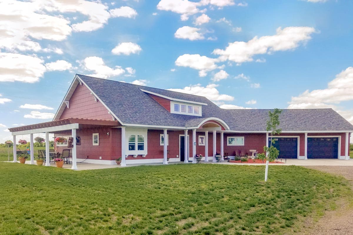 House plan exterior. Two-story, ranch-style home with a pergola, gable roof, dormer, and attached garage. Red siding with white trim.