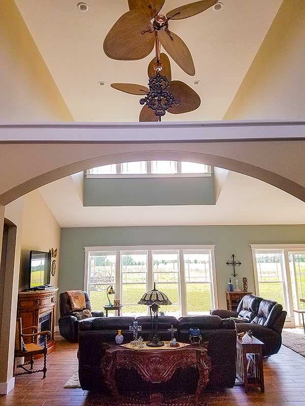 Interior view of great room with vaulted ceiling, ceiling fan, fireplace, large windows, and open layout.