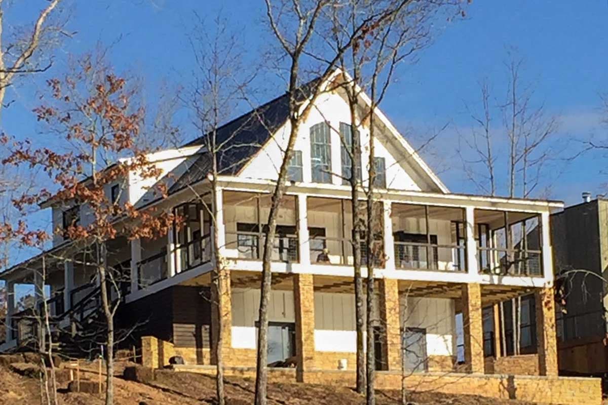 House plan exterior showing a multi-story Modern Farmhouse with a wrap-around porch, gables, dormers, and stone foundation.