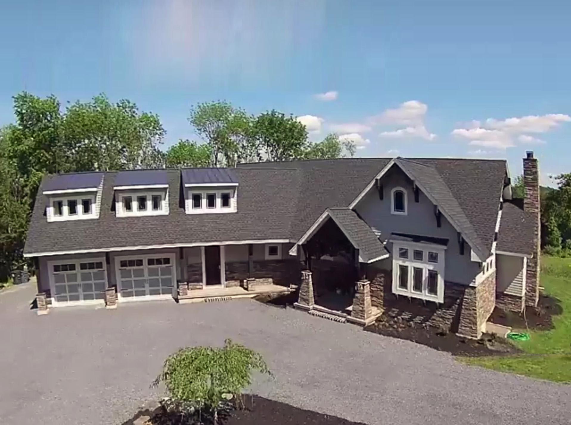 House plan exterior featuring a three-car garage, prominent gabled dormers, stone accents, and a covered entry porch with stone pillars.
