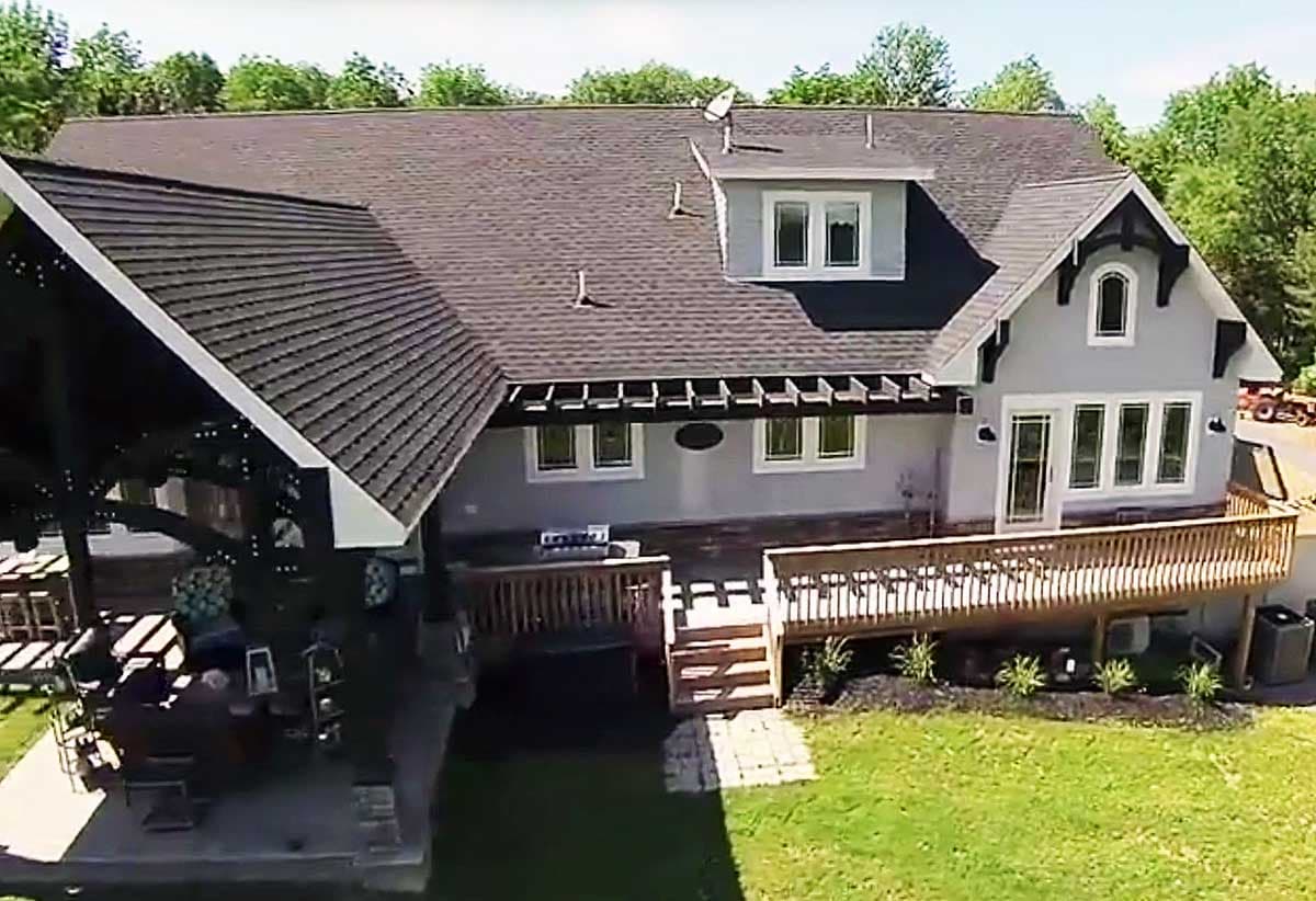 House plan exterior: Two-story dwelling with large wraparound deck, covered patio, and multiple gables.