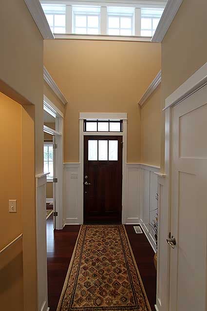 Interior view of a hallway with a dark wood door, transom window, and a runner rug on hardwood floors.
