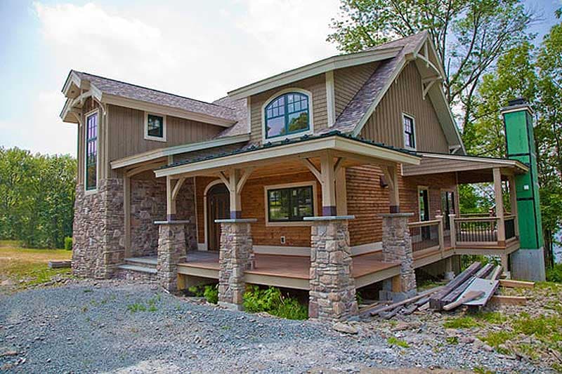 House plan exterior: two-story home with stone and wood siding, covered porch with stone pillars, and gabled dormers.