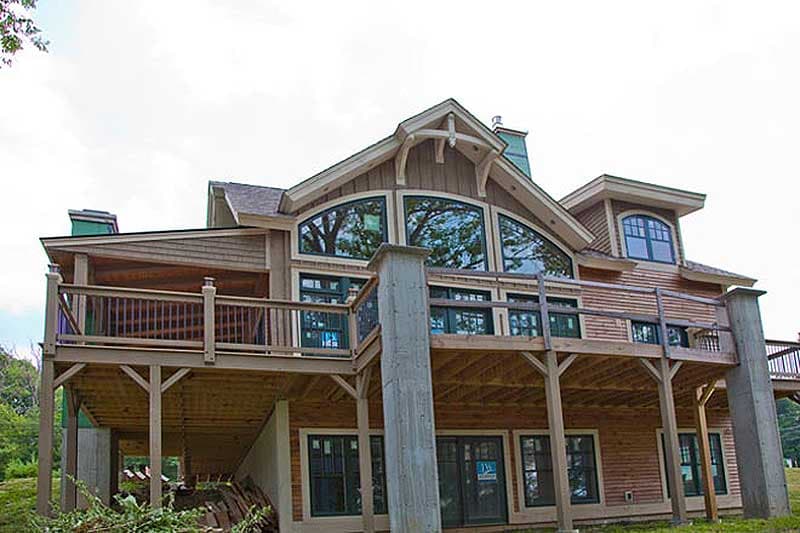 House plan exterior with a multi-story design, wooden shingle siding, gables, large arched windows, and extensive decks.